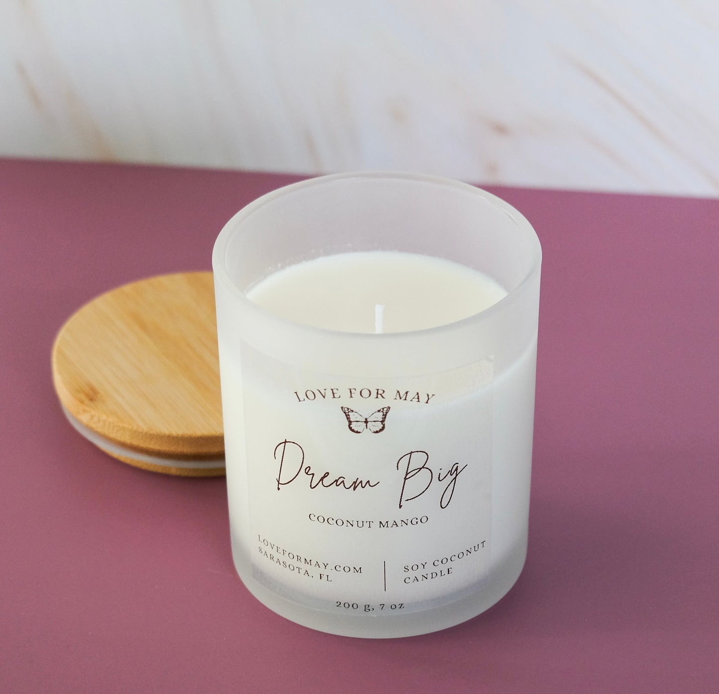 Coconut Mango scented candle in a frosted glass jar with a bamboo lid and the words dream big on the label.