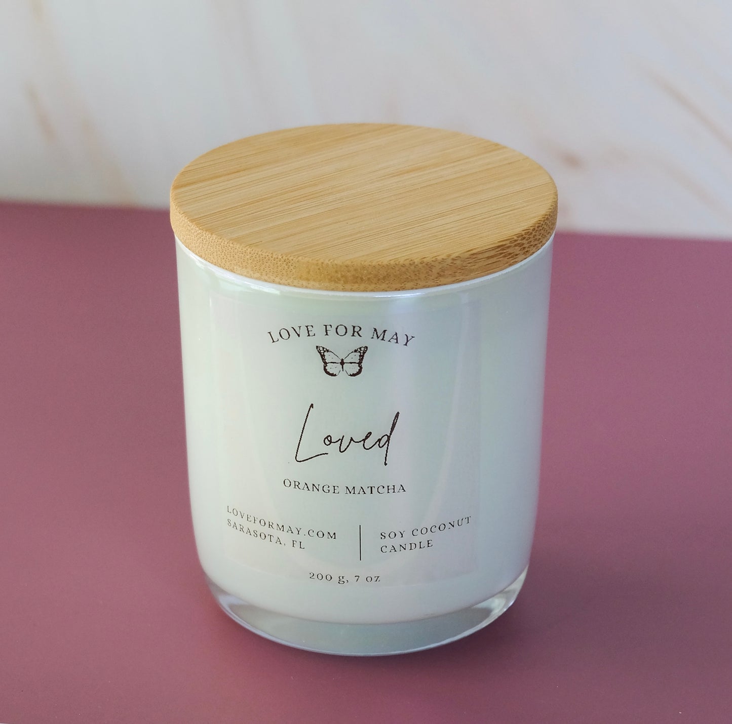 Orange Matcha scented candle in a white iridescent glass jar with a bamboo lid and the word loved on the label.