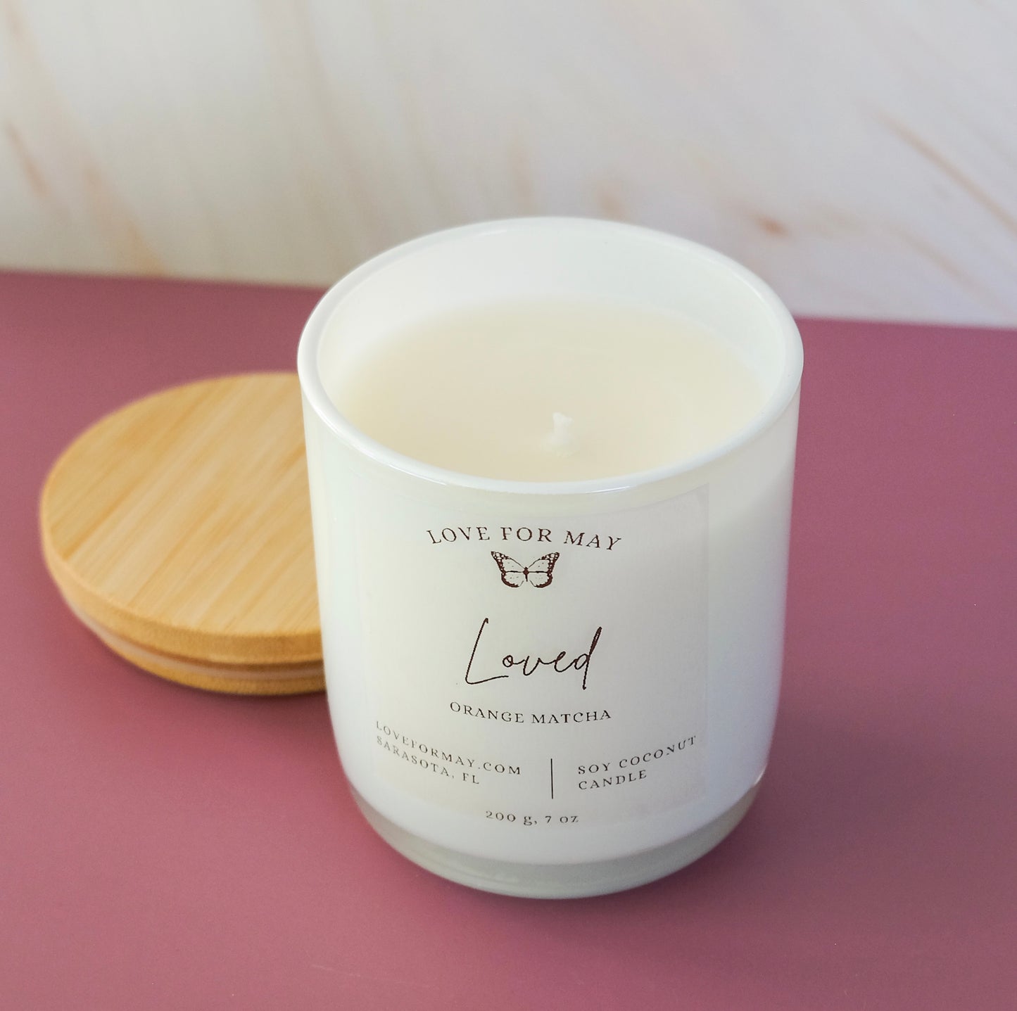 Handmade candle in a white iridescent glass jar with a bamboo lid and the word loved on the label.