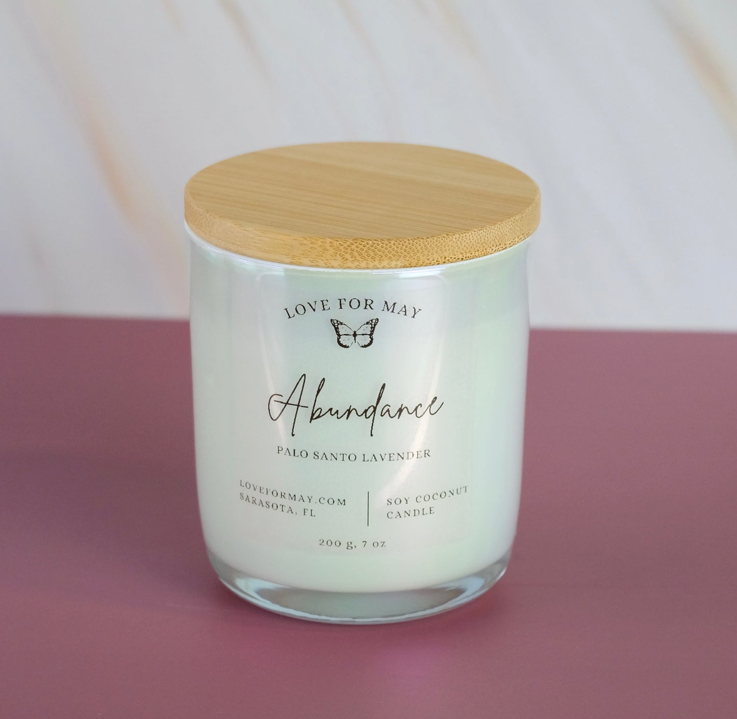 Palo Santo Lavender scented candle in a white iridescent glass jar with a bamboo lid and the word abundance on the label.