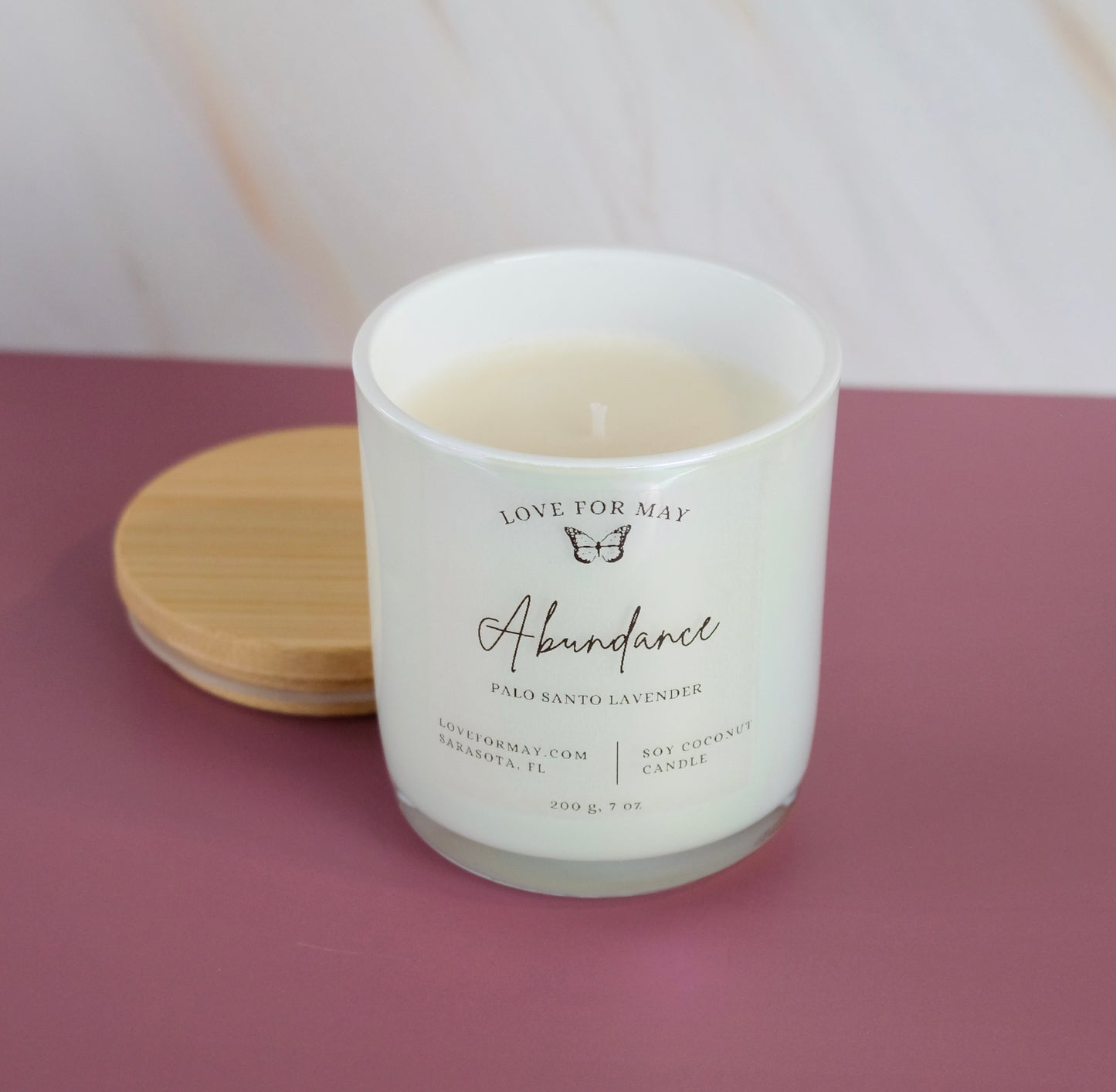 Palo Santo Lavender scented candle in a white iridescent glass jar with the word abundance on the label.