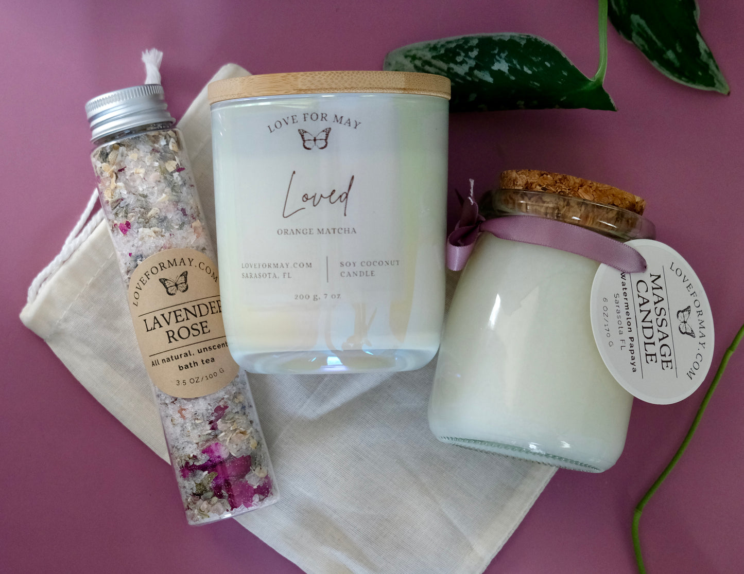 A tube of rose lavender bath tea and bath salts, an iridescent manifestation candle with the word Loved on the label, and a massage candle