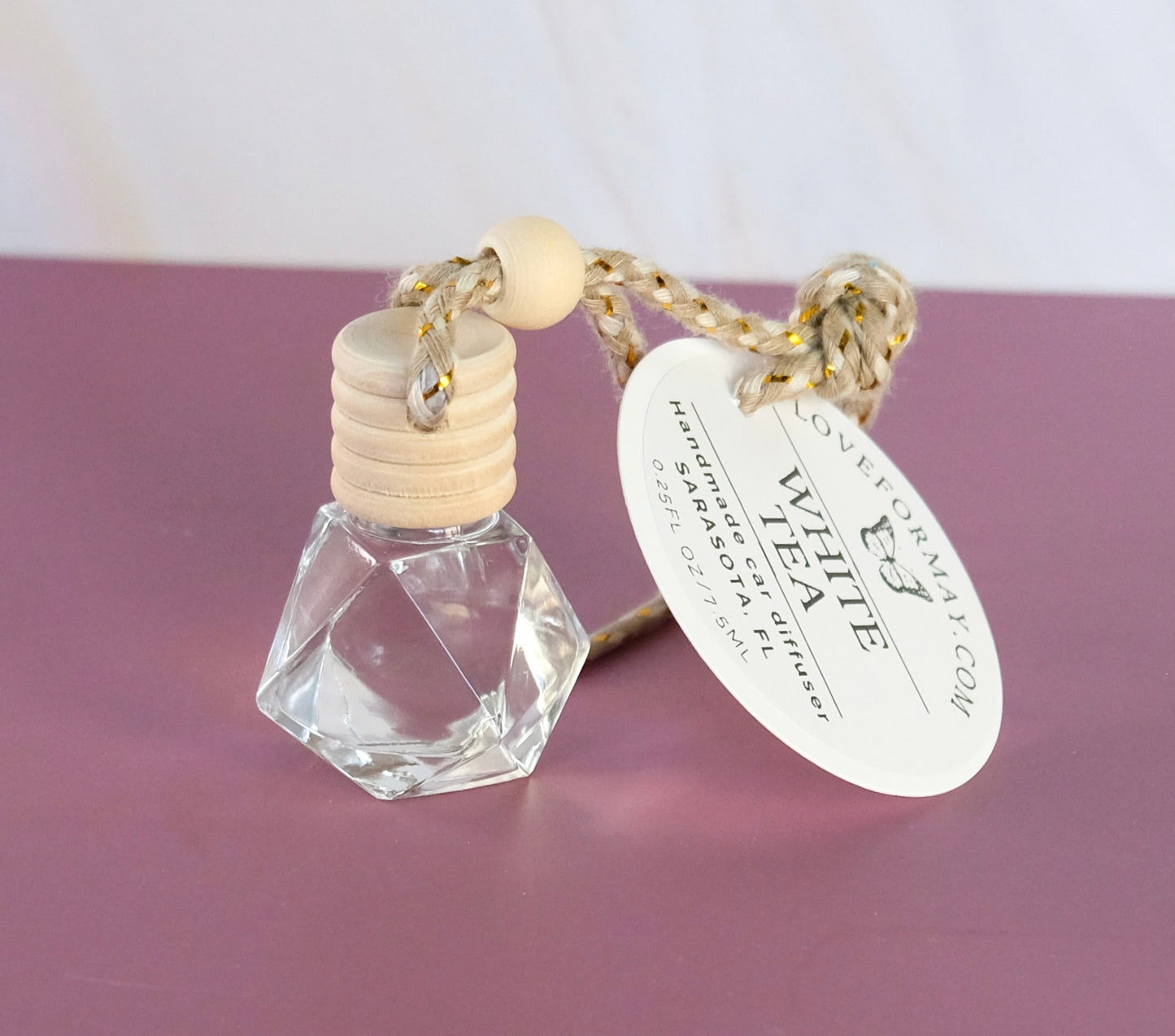White tea car diffuser in a diamond shaped glass bottle with a wood lid and a string
