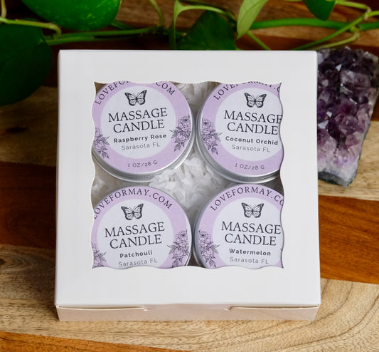 Four massage candles in a box with purple labels on a wooden surface.