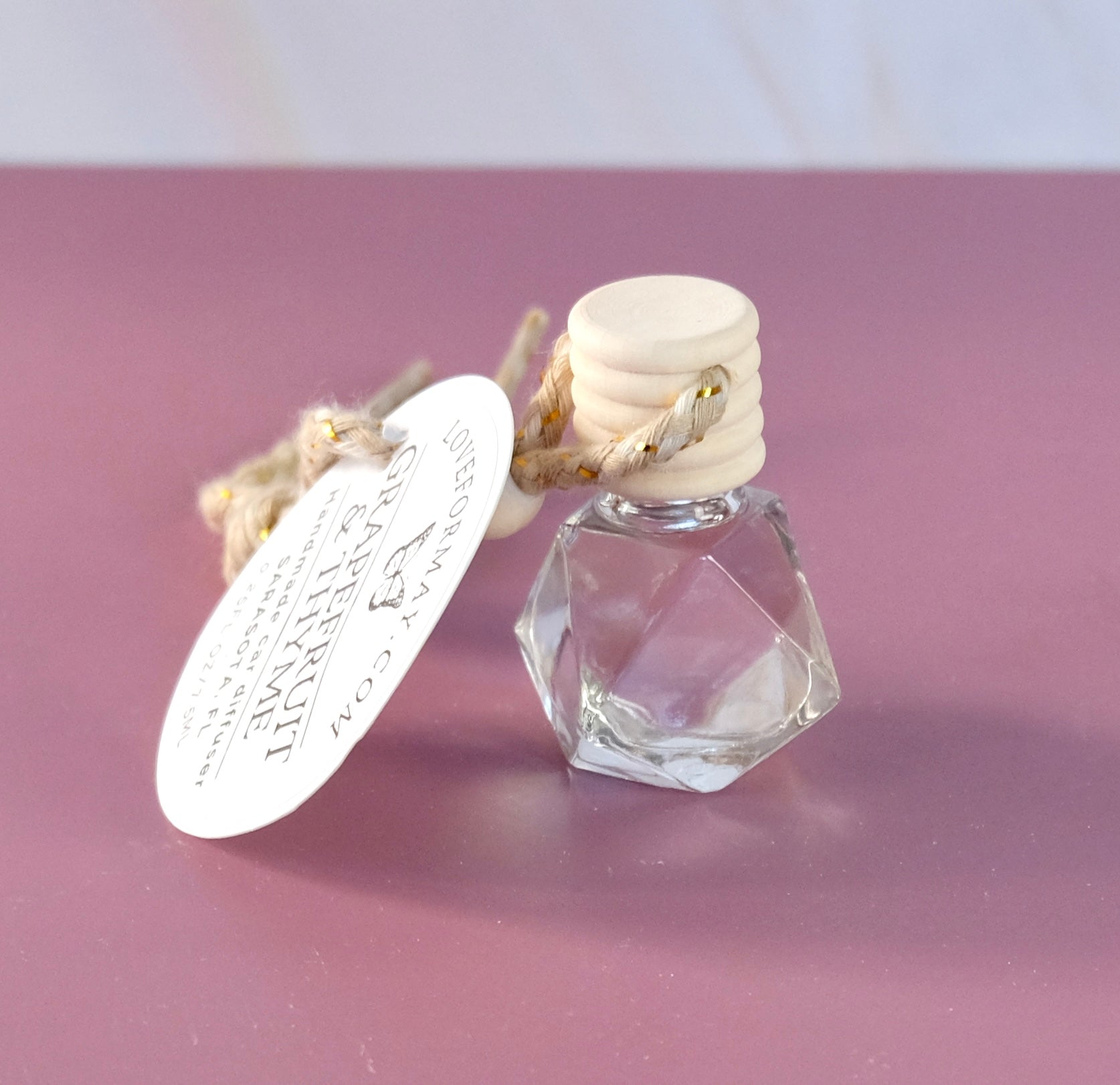 Grapefruit & Thyme scented car diffuser in a diamond shape glass bottle with a wood lid and a string.