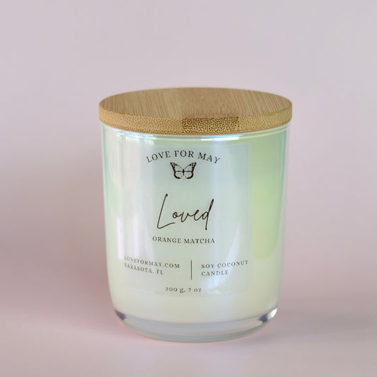 Orange Matcha scented candle in a white iridescent glass jar with a bamboo lid and the word loved on the label.