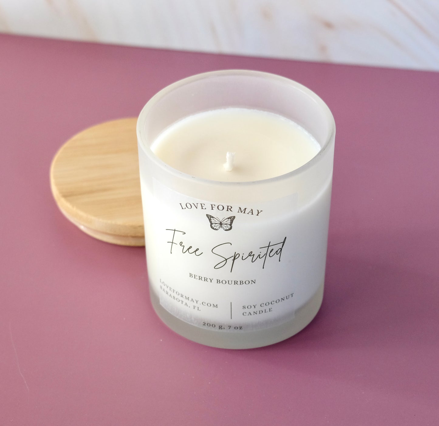Frosted glass container candle with a bamboo lid, the words Free Spirited on the label and scented Berry Bourbon.