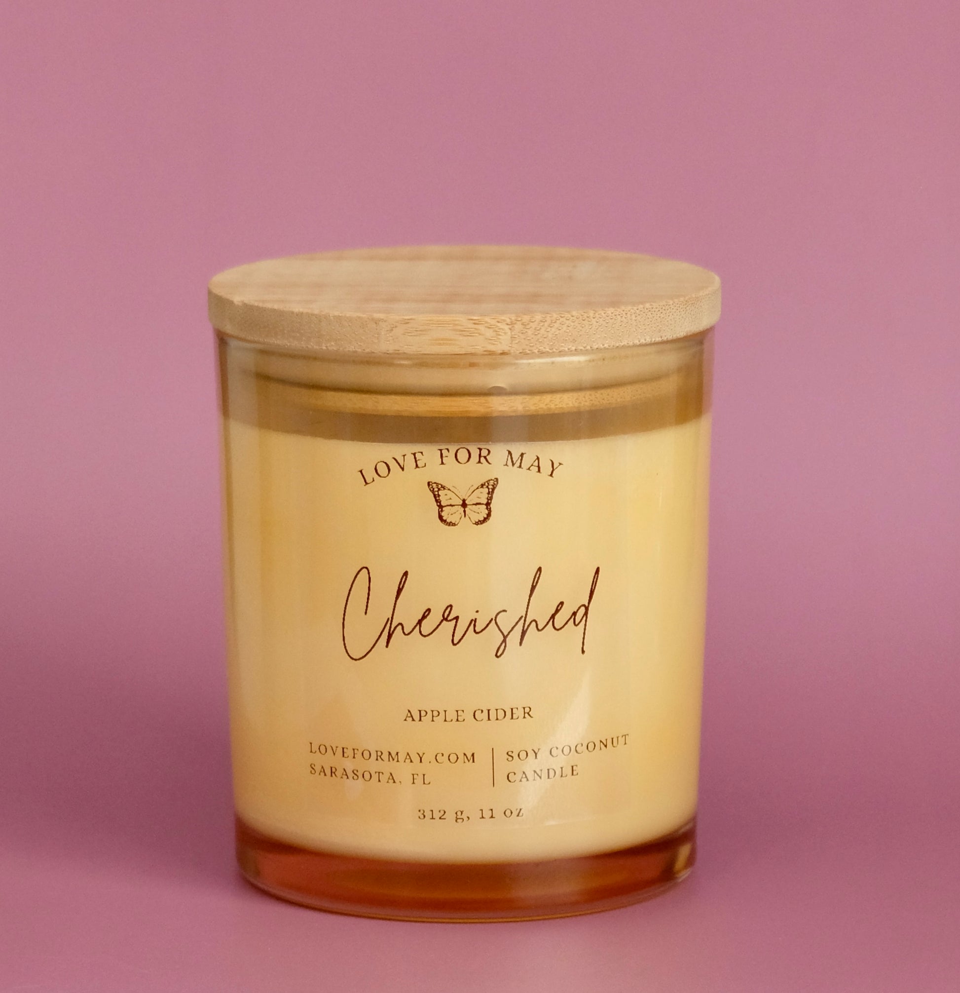A light amber glass container candle with a wooden lid and the affirmation Cherished.
