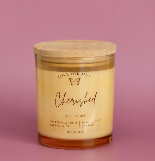 A light amber glass container candle with a wooden lid and the affirmation Cherished.