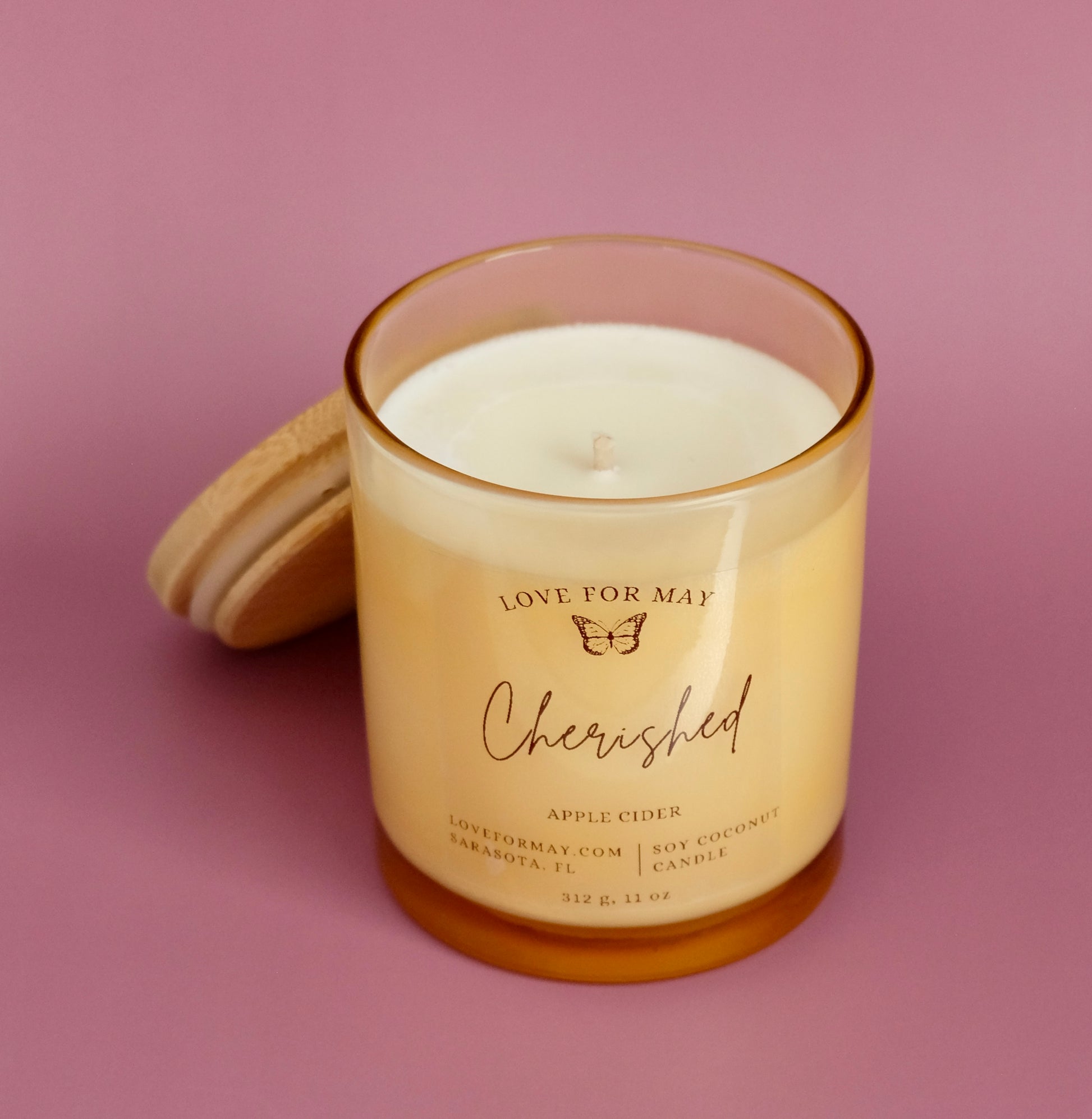 A light amber glass container candle with a wooden lid and the affirmation Cherished.