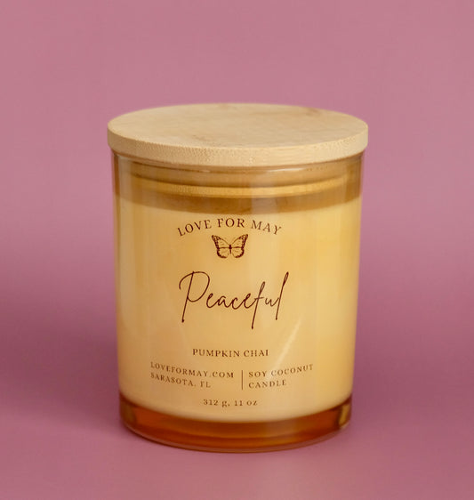 Light amber glass container candle with a wooden lid and the word peaceful on it