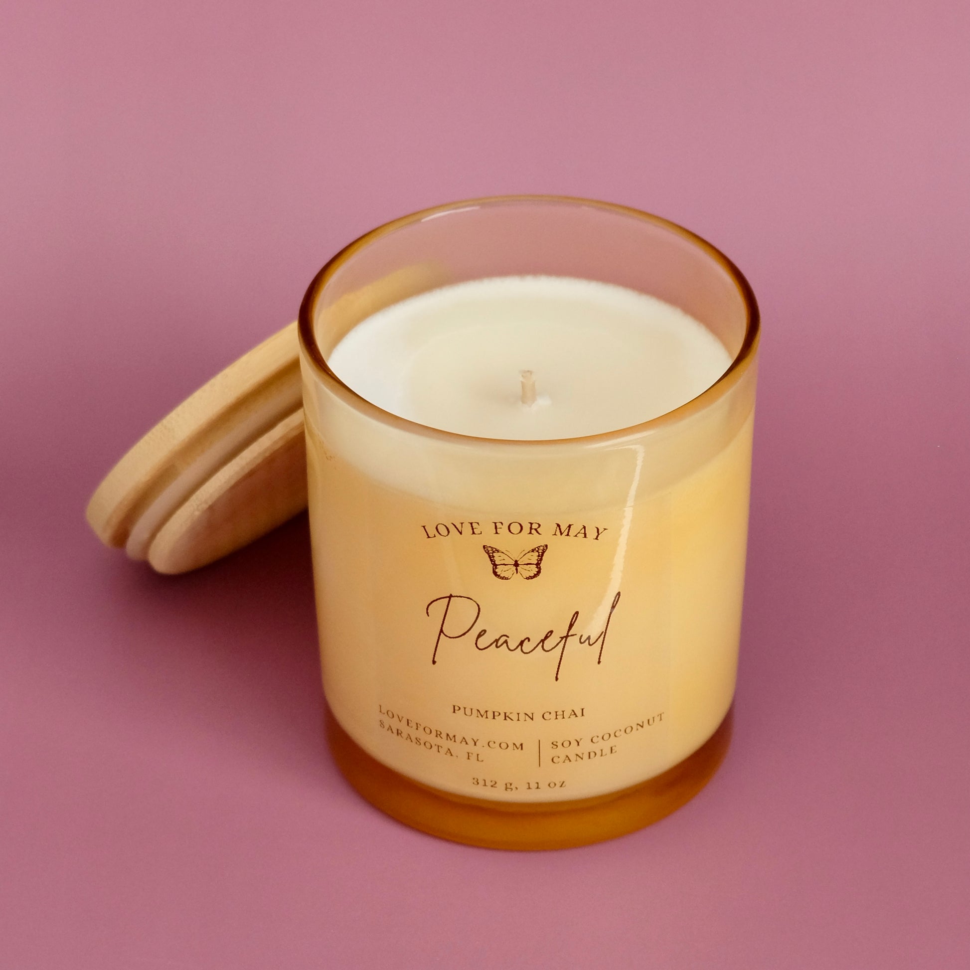 Light amber glass container candle with a wooden lid and the word peaceful on it