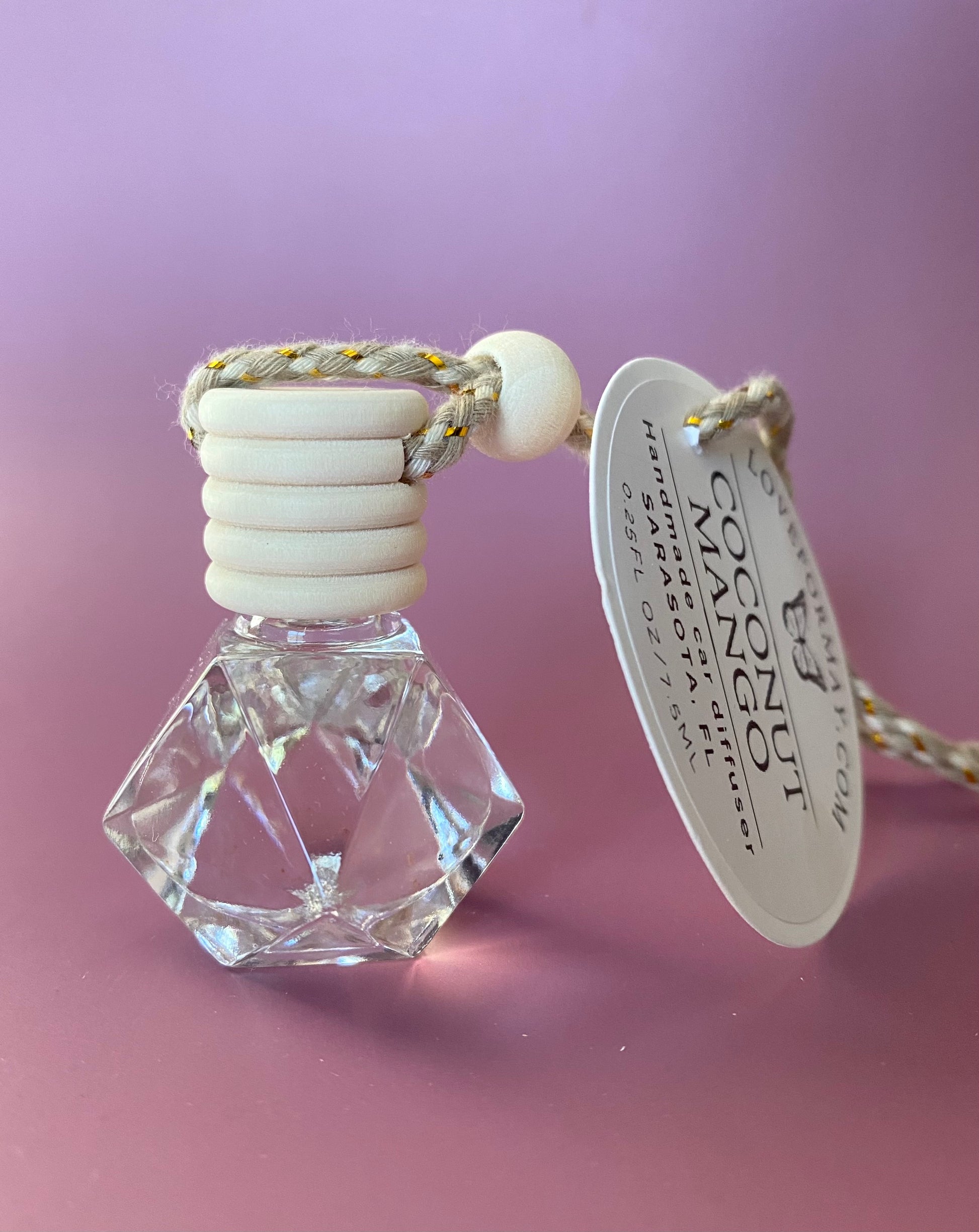 Coconut mango scented car diffuser in a diamond shape glass bottle with a wood lid and a string.