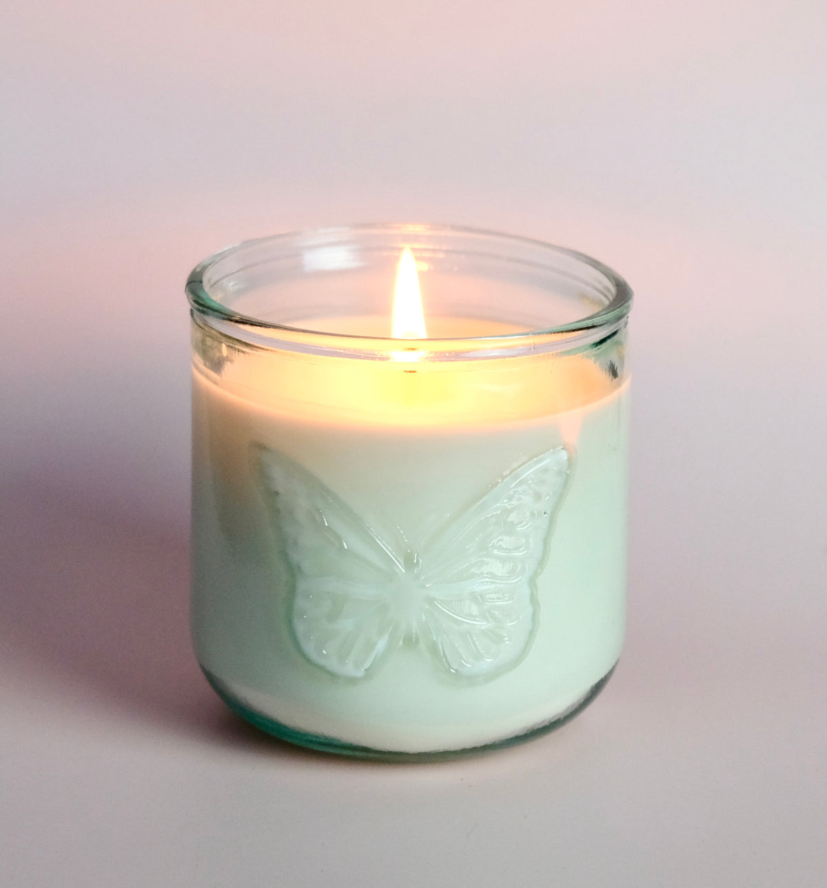 Lit candle in a glass jar with a butterfly design on a light background