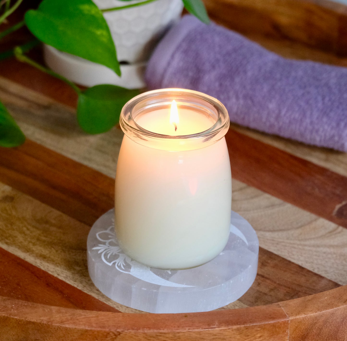 Massage candle in a glass jar on a wooden surface with a plant and towel in the background