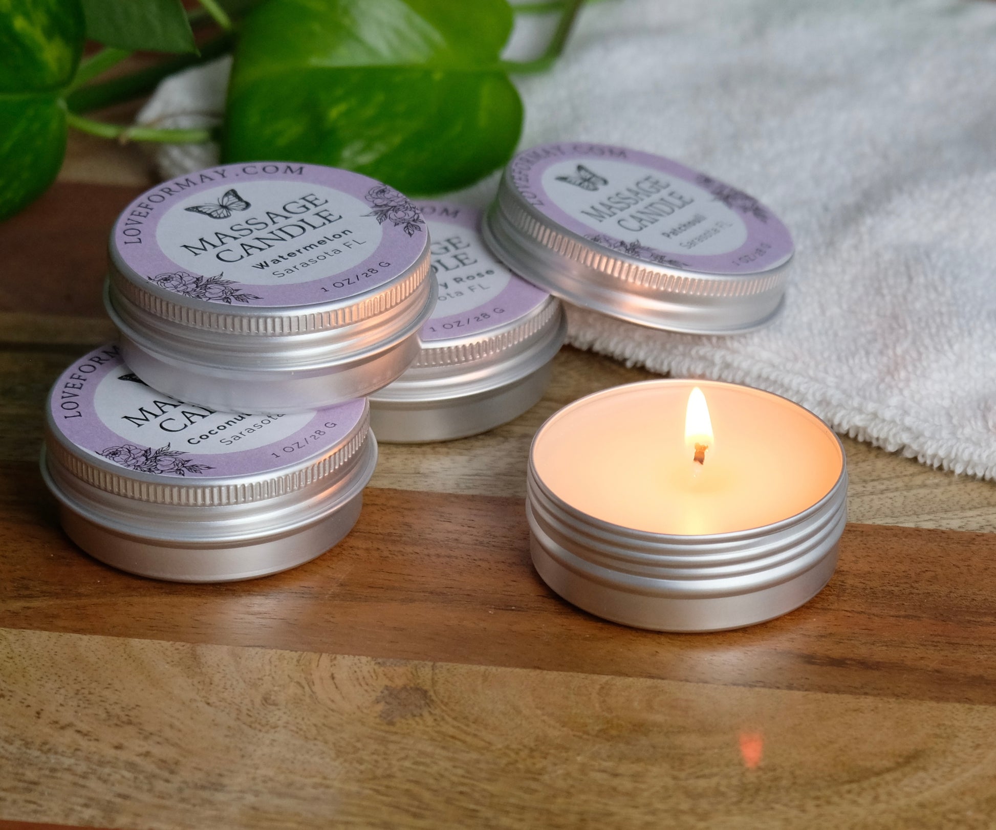 Stack of massage candles with a lit candle on a wooden surface.