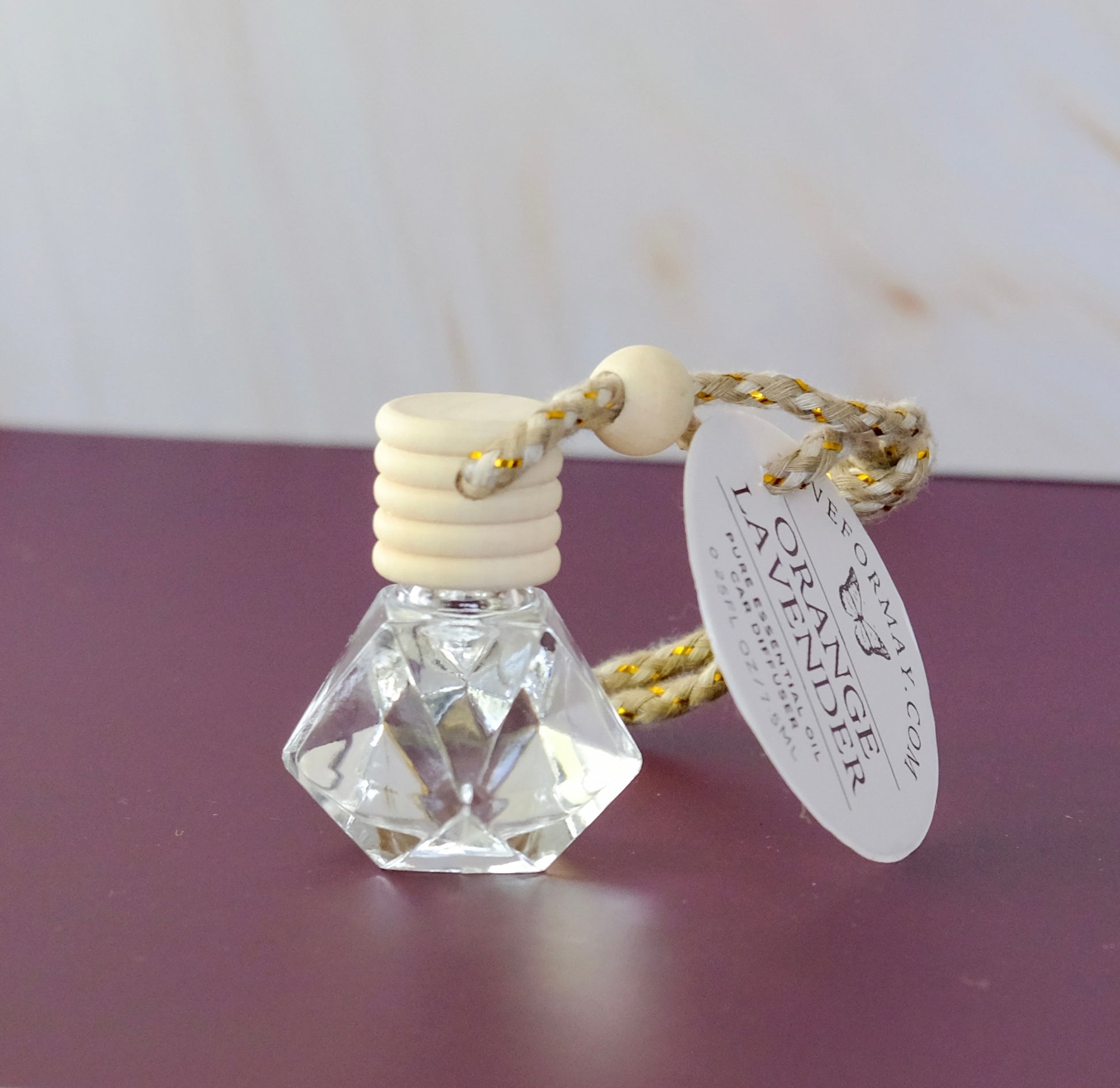 Orange lavender essential oil car diffuser in a diamond shape glass bottle with a wood lid and a string.