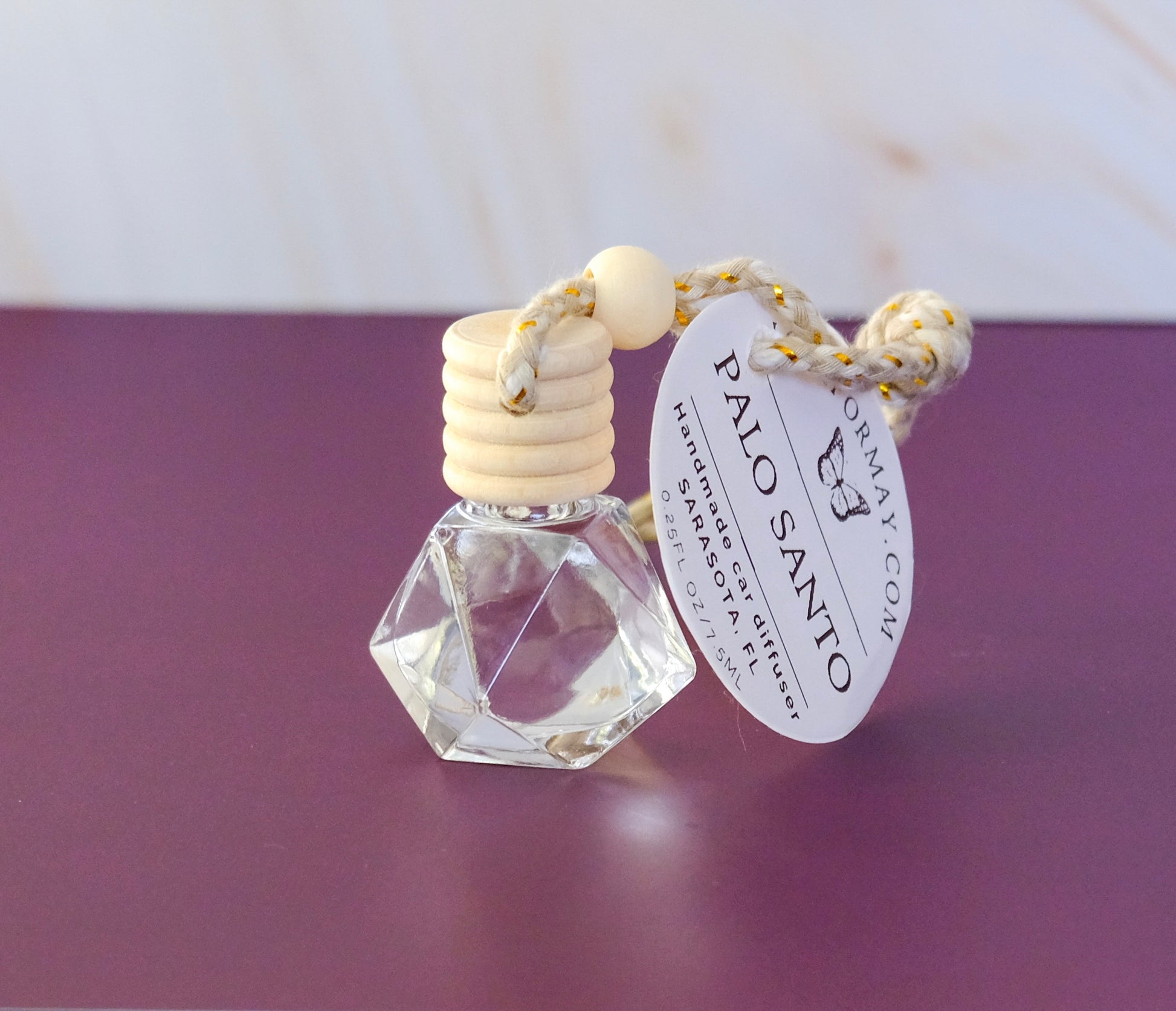 Palo Santo scented car diffuser in a diamond shape glass bottle with a wood lid and a string.