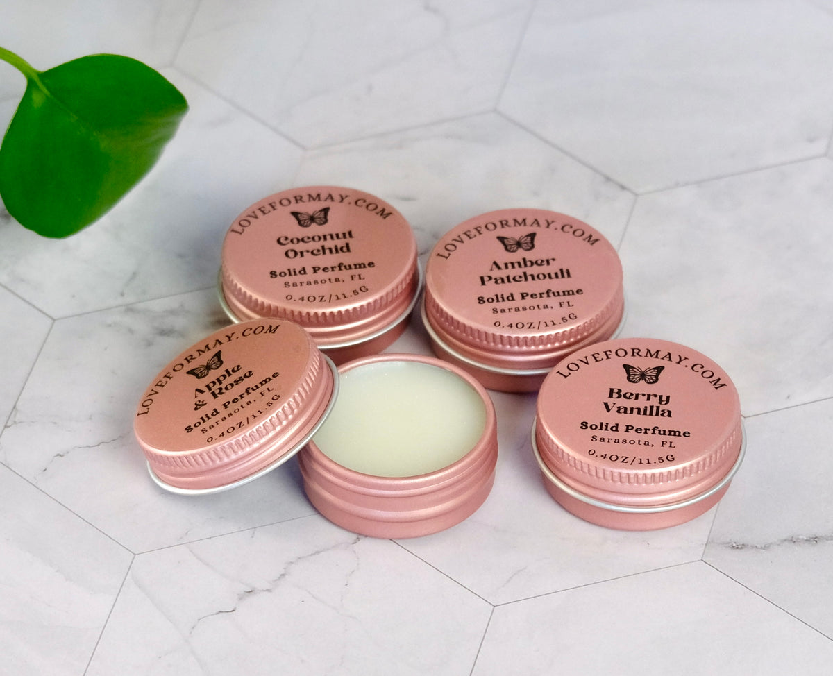 Pink solid perfume containers with labels on a white marble surface.