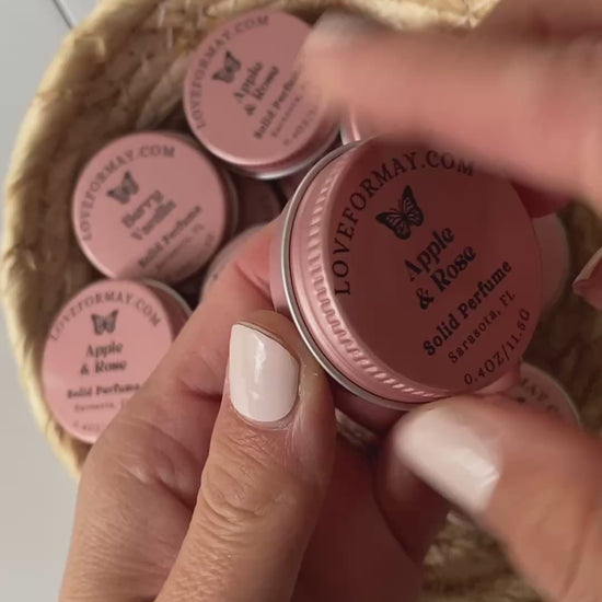 Hands unscrewing the lid on a pink solid perfume