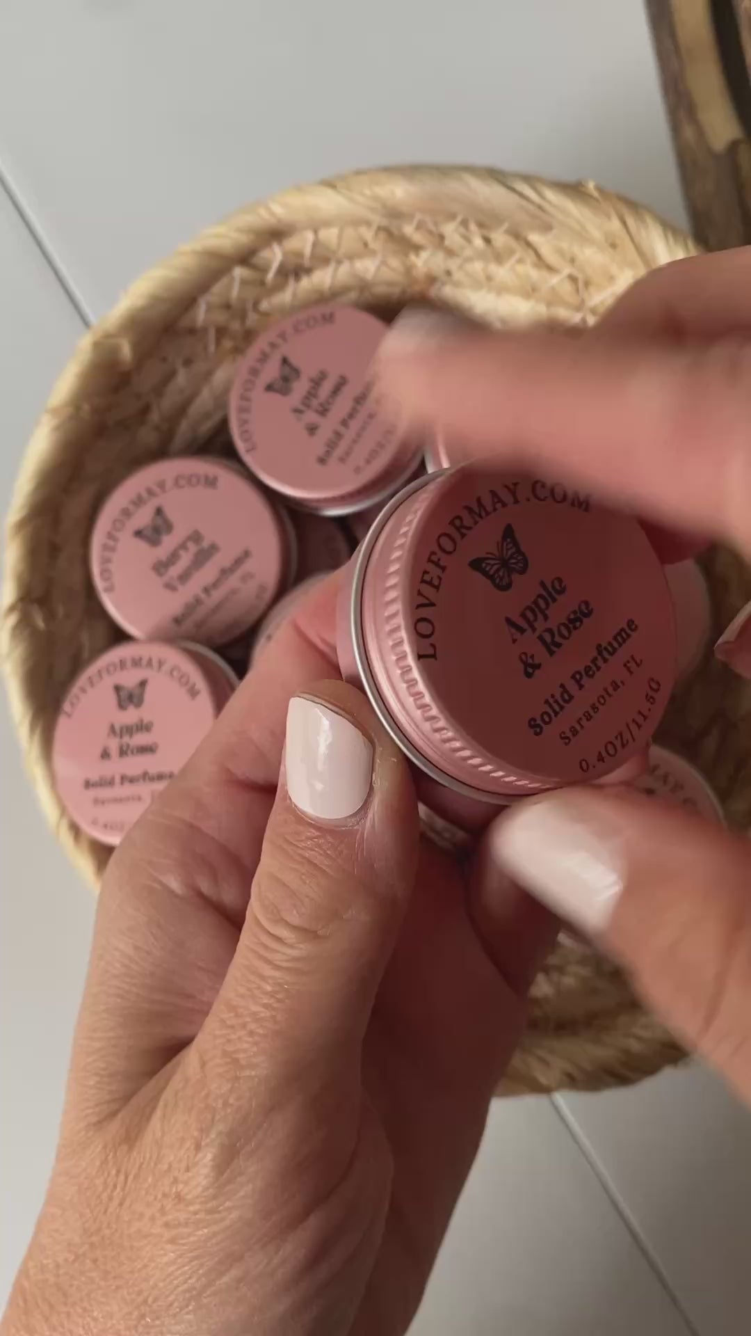 Hands unscrewing the lid on a pink solid perfume